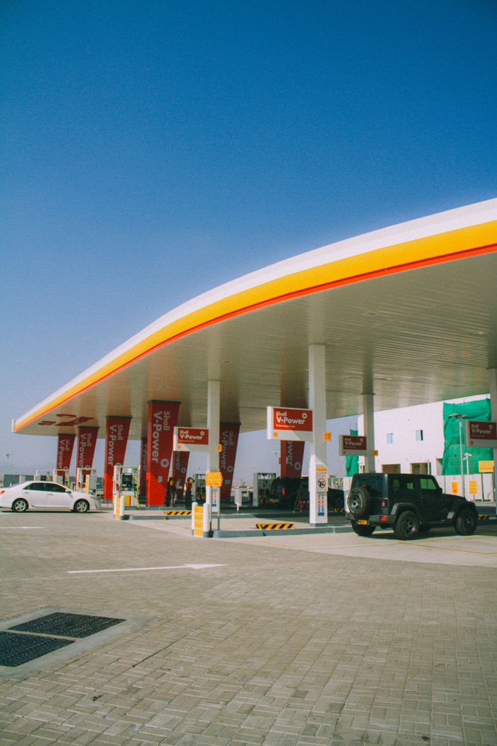 Sunlit Shell gas station in Muscat, Oman with vehicles refueling under a clear blue sky.