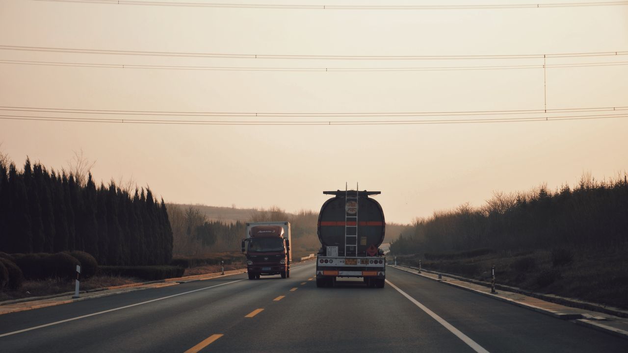 Long haul trucks traveling on a highway during sunset with a serene backdrop.